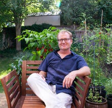 Jan sitting on a wooden bench outside with his pepper plants