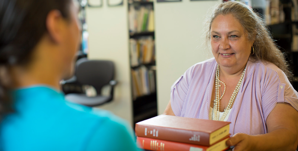 A staff member hands books to a patron at the Dana Porter library circulation desk.