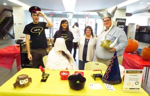 Library staff dressed in Halloween costumes stand behind a table.