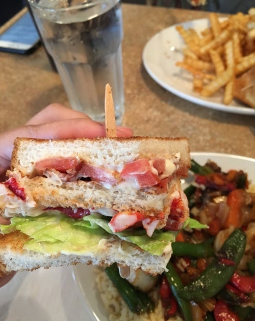 A hand holding a large lobster club sandwich.