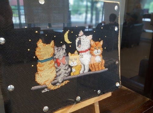 Cross stitch of a group of cats on a black background.