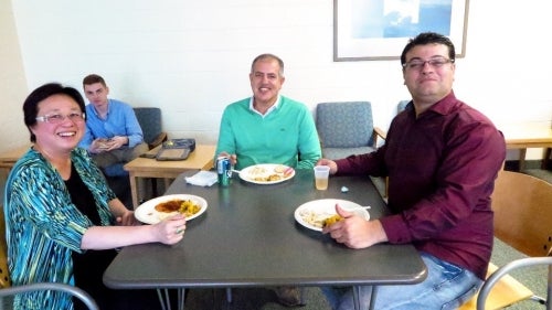Three staff members sit at a table with plates of food in front of them.