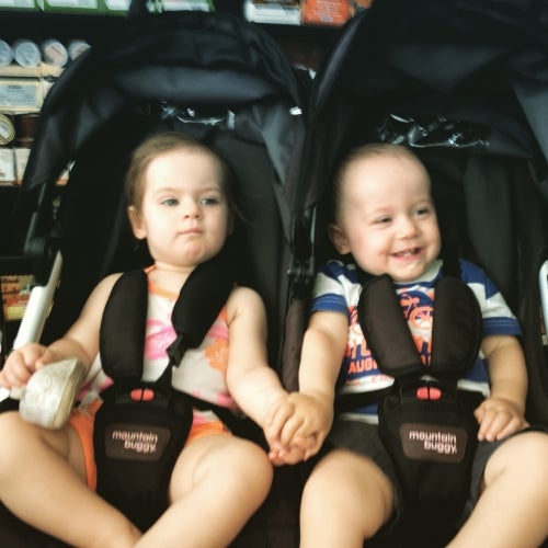 twin babies holding hands in a stroller