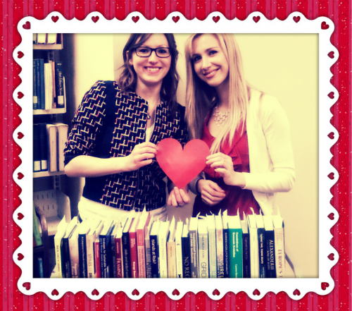 Two cataloguers standing in front of a book truck filled with books and holding a red heart.