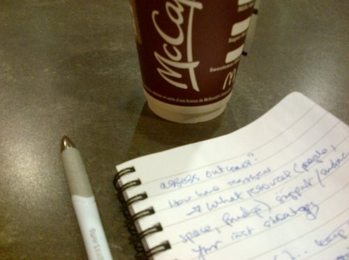 Coffee cup, pen, and spiral notebook with writing.