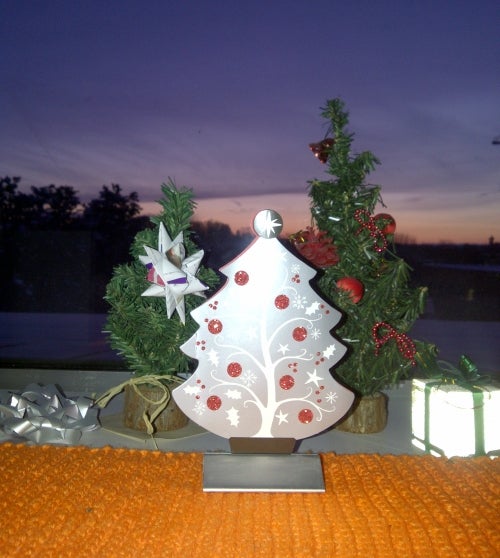 Christmas trees on a shelf in front of a window with the sunset in the background.