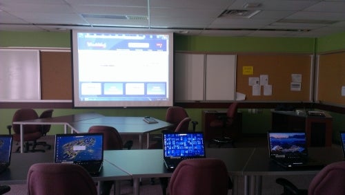 A room set up for training with several laptops and a large screen.