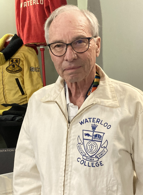 The front left-side of the jacket features a design printed in blue that includes the school’s name, “Waterloo College,” the Waterloo College coat of arms, and the Waterloo College motto “Veritas omnia vincit.”