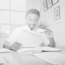Image of Toks Oshinowo sitting at a desk and reading The Enginelus while holding a pair of glasses.