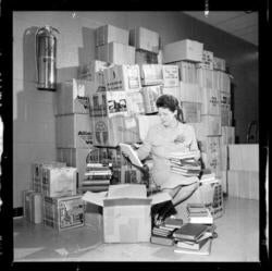 Doris Lewis seated in front of a stack of boxes reviewing books from an opened box.