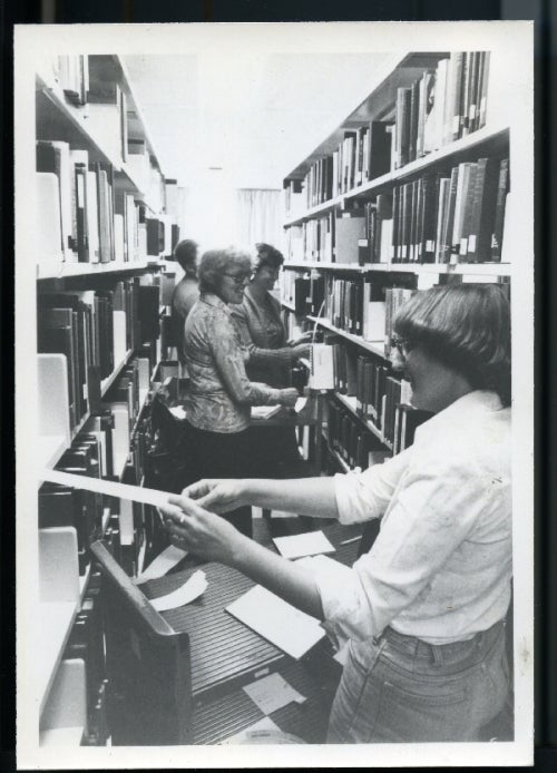 Library staff barcoding books in the stacks