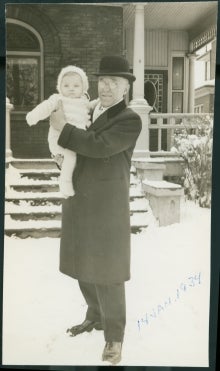 Man holding baby standing in front of house.