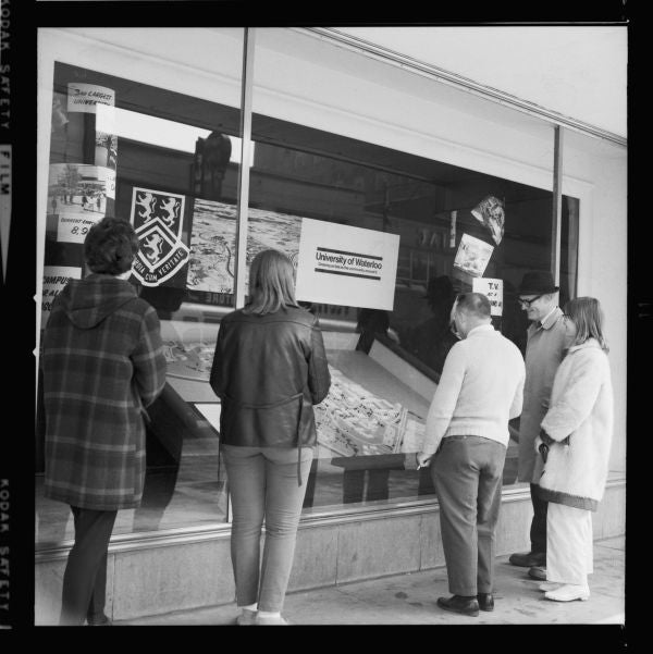 People gathered around a display case containing some University of Waterloo promotional material and a 3D model of campus