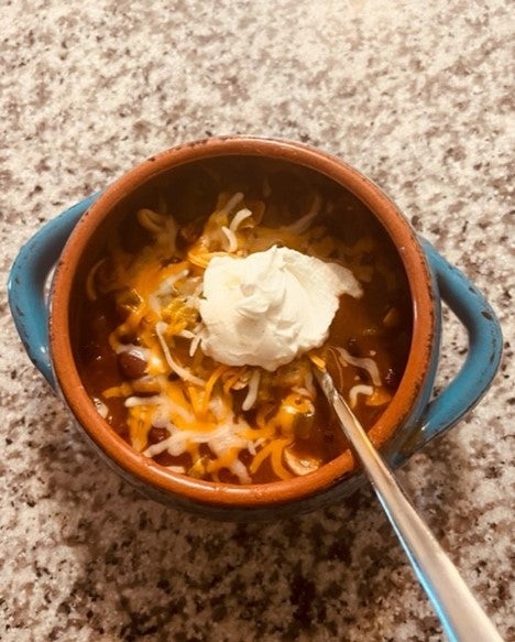 Small round bowl with cheese and sour cream topped chili and a spool inside