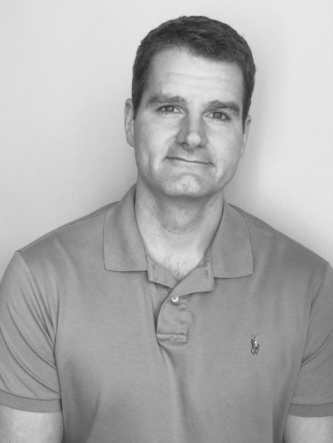 A black and white photo of a man in a polo shirt smiling at the camera