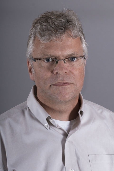 Man with an off-white shirt and grey background looking at the camera