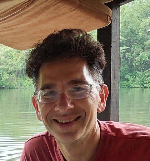 Man with glasses and short hair smiles at camera with pond and greenery background
