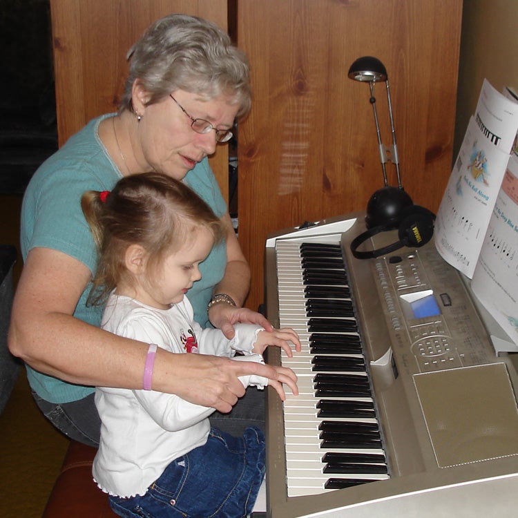 Older adult teaching child to play piano.