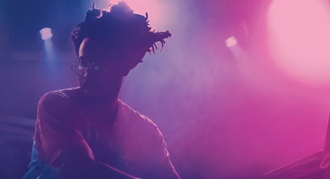 Chris Wilson performing behind the decks as he is lit by purple lights and fog.