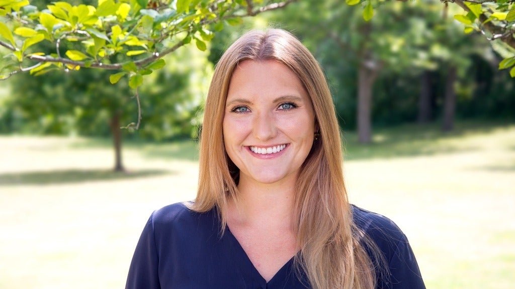 Kelly, with long blonde hair, wearing a blue shirt. Smiling.