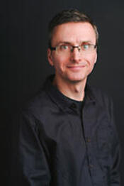 headshot of man wearing a black shirt, glasses and smiling