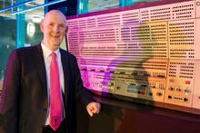 man wearing a suit with a pink tie standing beside an old computer