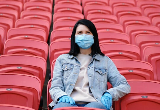 young woman sitting in an empty stadium wearing a medical mask