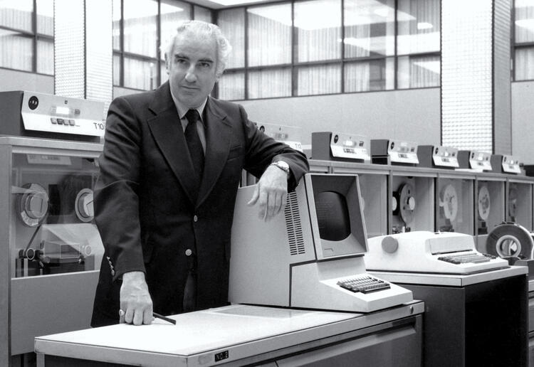 man with white hair leaning on an old computer 
