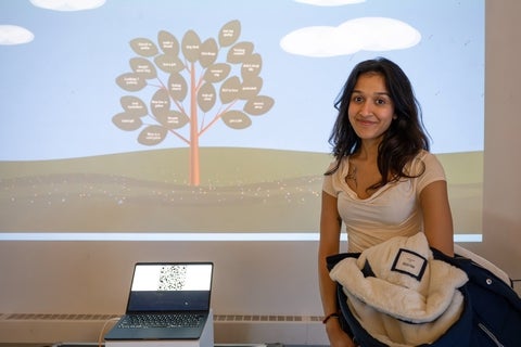 Someone standing in front of a projection of a tree with a laptop displaying a QR code besides them