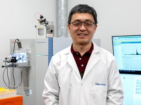Bin Ma in front of mass spectrometry machine