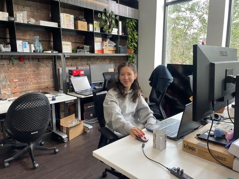 Person with long curly hair, sitting at a desk on a computer