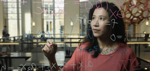 Women writing math equation on window
