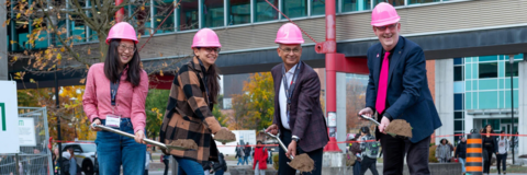 Four people with pink hard hats and shovels 