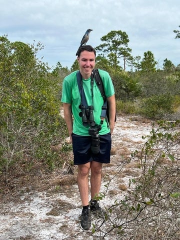 Ronen wears hiking clothes; a blue and white bird is perched on his head 