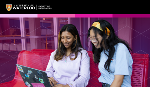 Two female students smiling and laughing while sitting on a bench and looking at a laptop