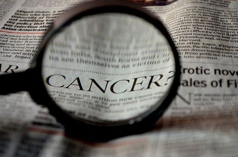 Magnifying glass being used to look at the word cancer in a newspaper.