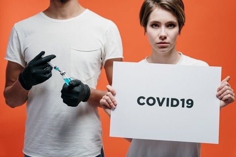 One person holding a syringe and another holding a COVID-19 sign