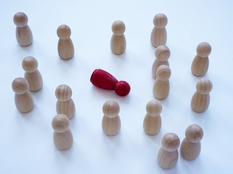 An image of wooden figures looking at a red wooden figure in the middle