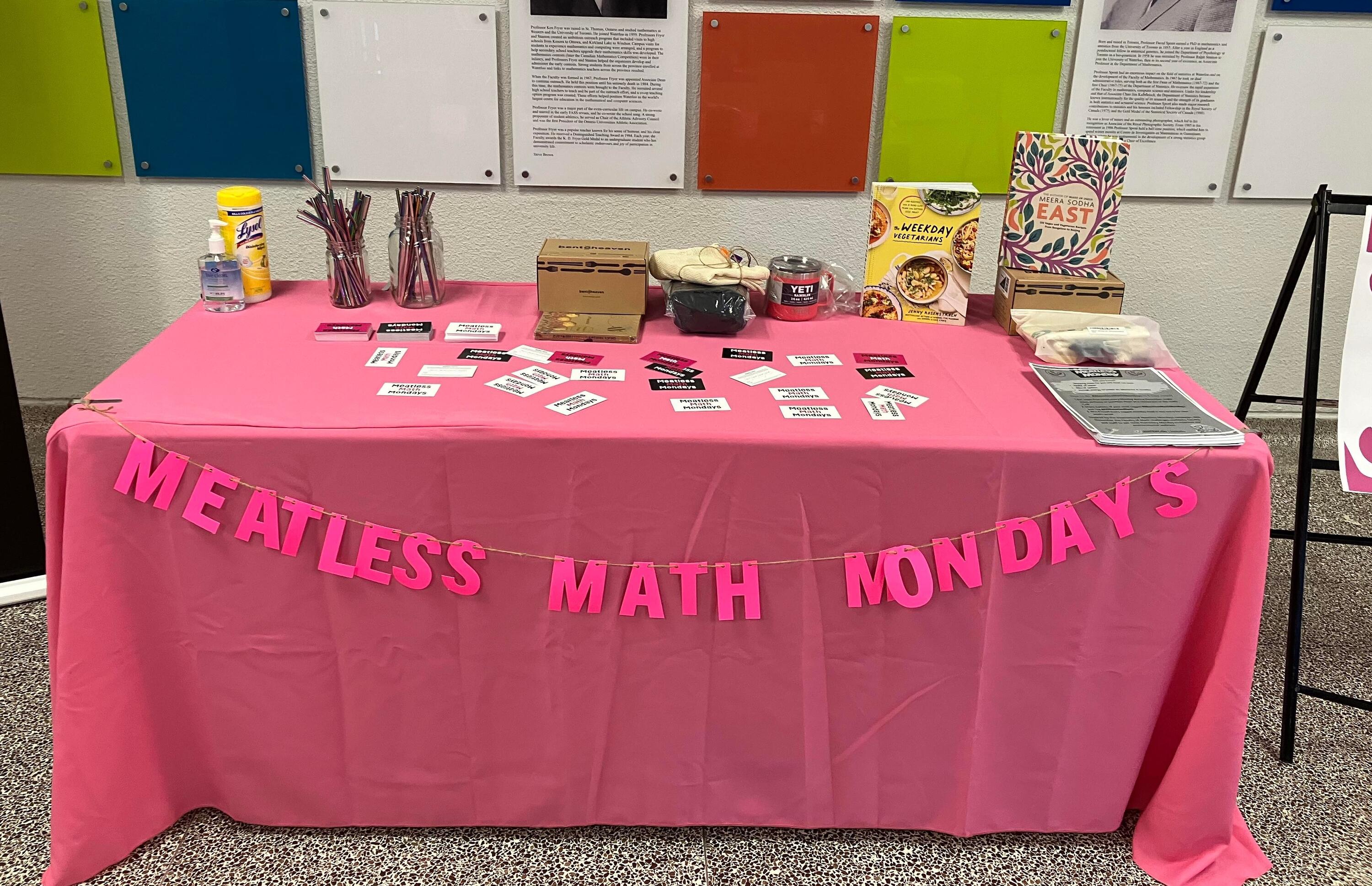A pink table covered in prizes and information sheets with a banner reading "Meatless Math Mondays"