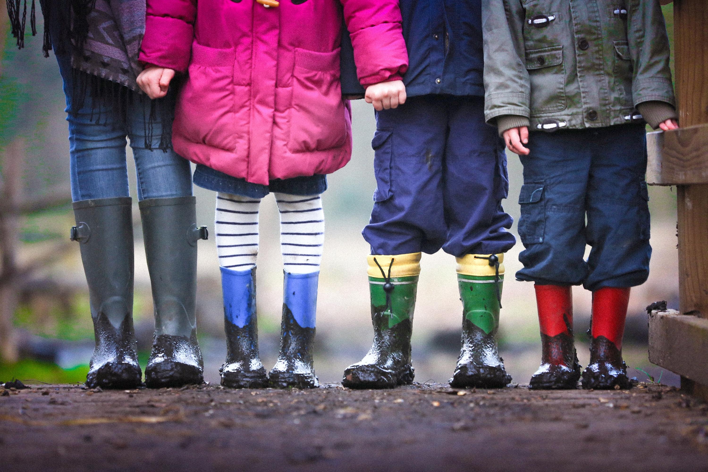 Four children wearing rainboots stand in the mud