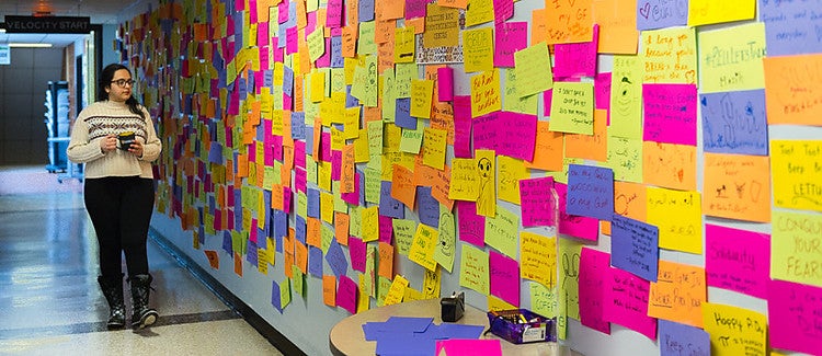 Student walking past a wall of post-it notes with messages written on them.