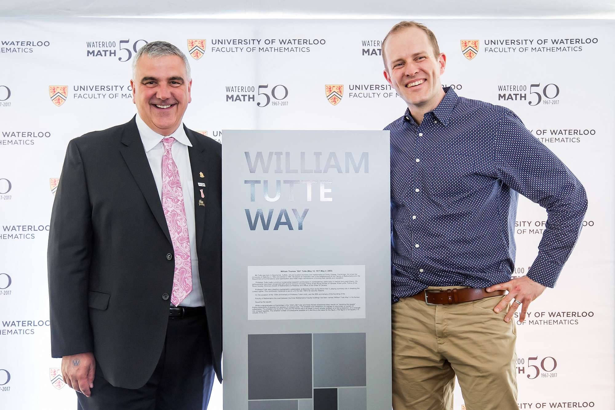 two men standing on either side of a sign smiling