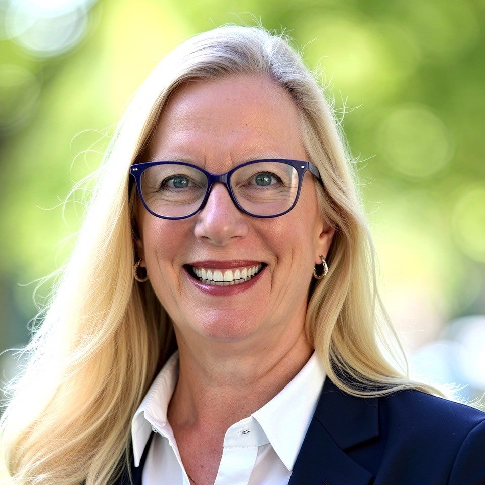 Headshot of a woman with long blond hair wearing glasses and smiling
