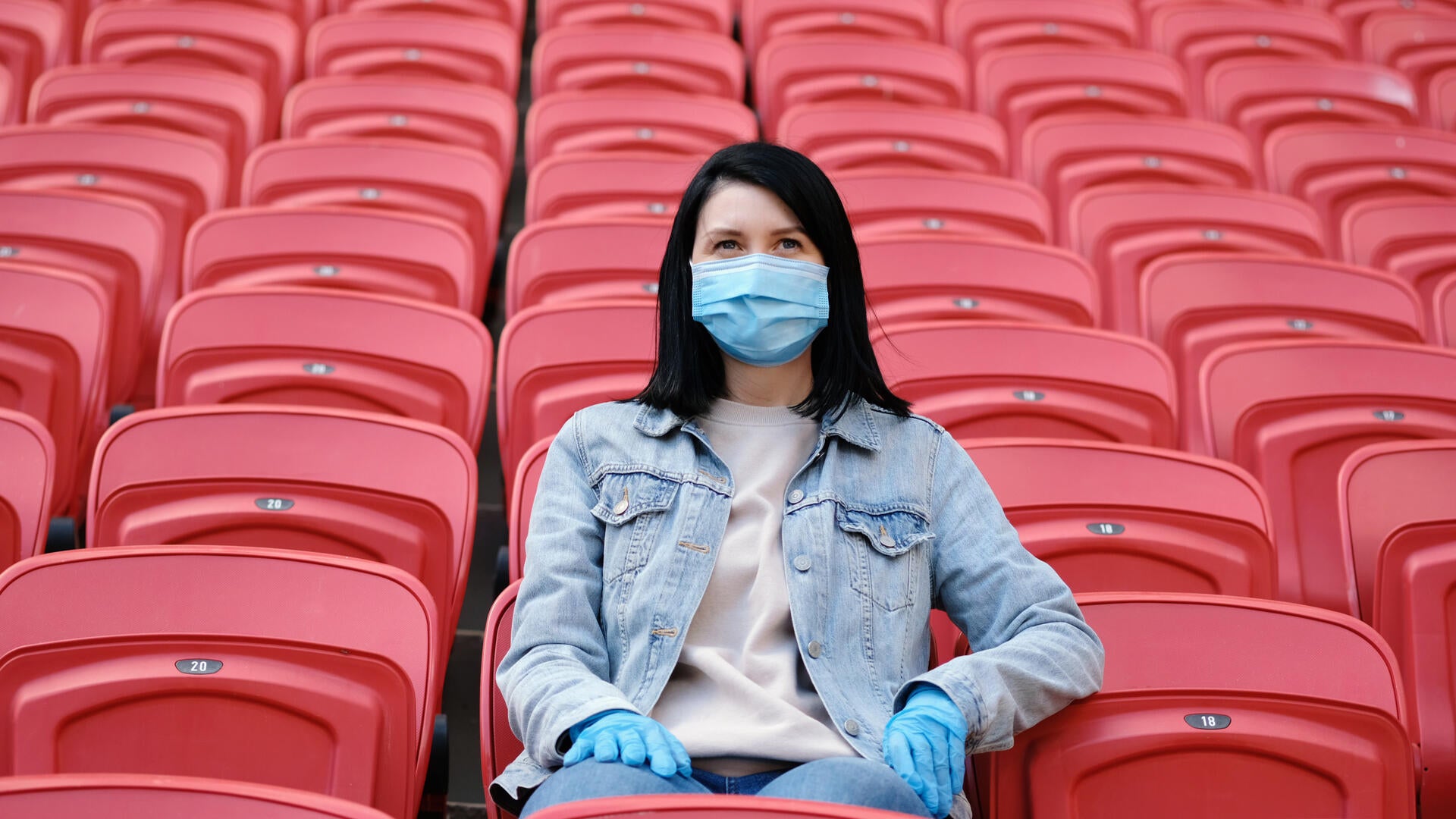 woman with dark hair wearing a mask sitting in an empty stadium