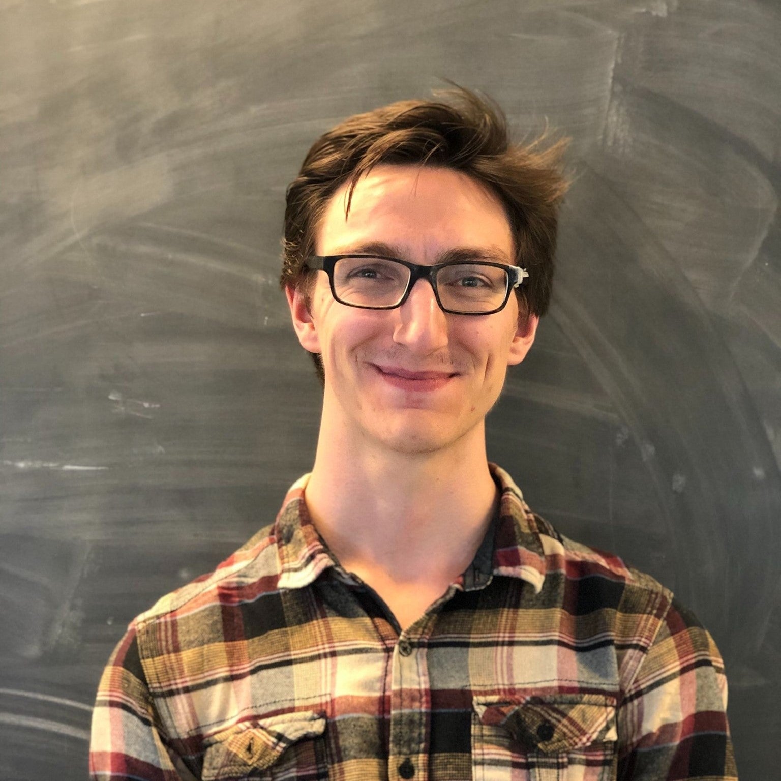 man with glasses standing in front of a chalk board