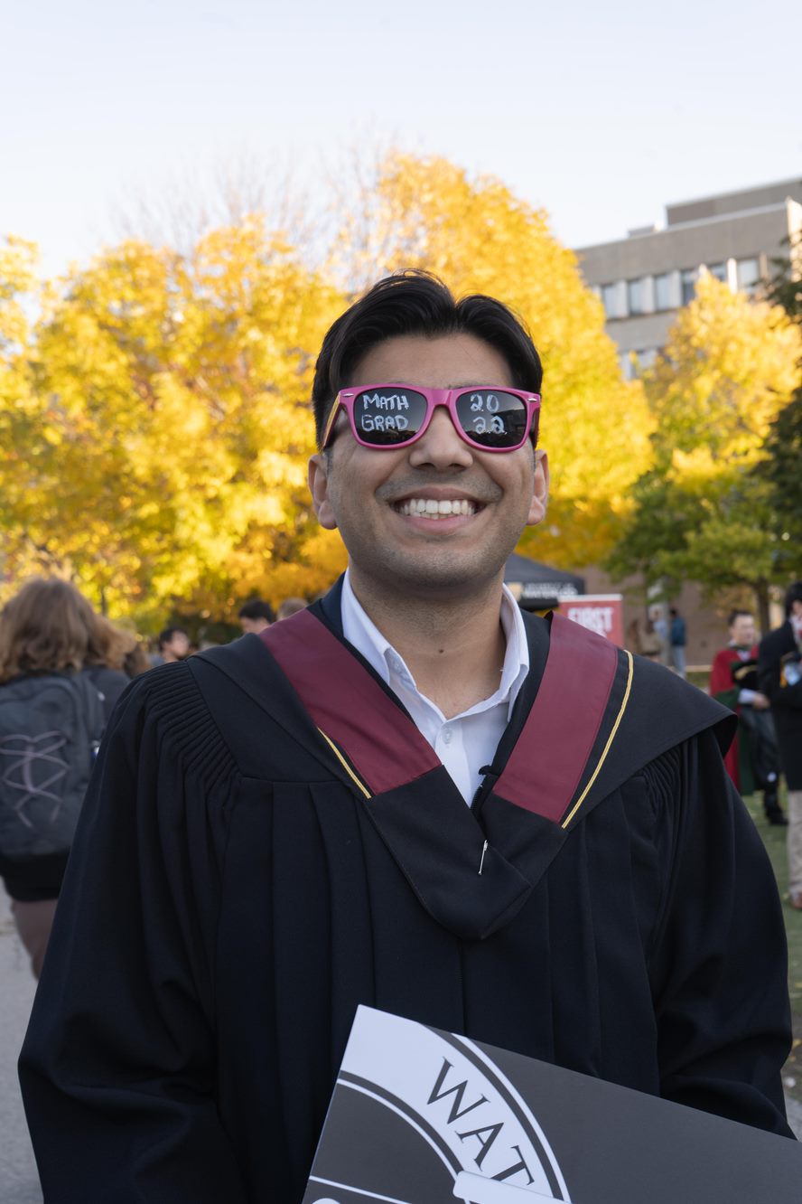 A student grins while wearing pink sunglasses and regalia