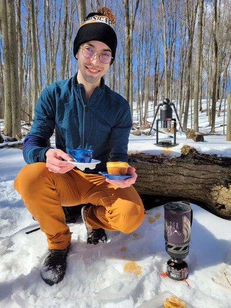 Jacob kneels in the snow holding a cup of espresso