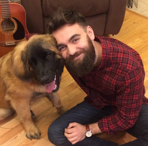 young man with a beard hugging a dog smiling
