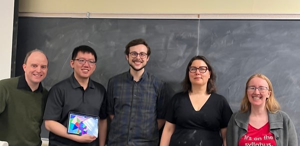 Group of math professors smiles in front of chalk board