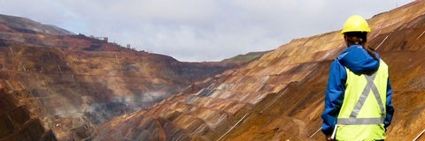 Person stands overlooking a terraced, open pit mine. 